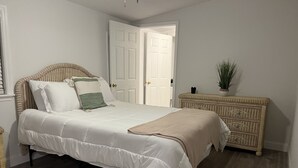 Un dormitorio con cama, cómoda, planta y puerta.