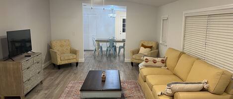 A living room with a sofa, armchairs, a coffee table, a TV, and a ceiling fan.