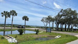 Una carretera con un cartel de Douglas C. Crane Boat Ramp, un área verde con un pequeño estanque y palmeras.