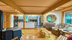 Un salón amplio con piso de madera, una cocina con armarios blancos, un espejo grande y un sofá de cuero.