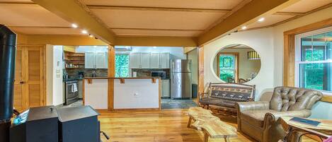A spacious living area with a wooden floor, a kitchen with white cabinets, a large mirror, and a leather sofa.