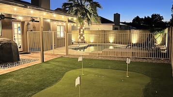 A backyard with artificial grass, a pool, and a fenced area.