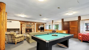 A pool table in a room with a fireplace, sofas, and a bookshelf.