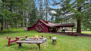 A cabin with a fire pit, picnic tables, and a covered area with benches.