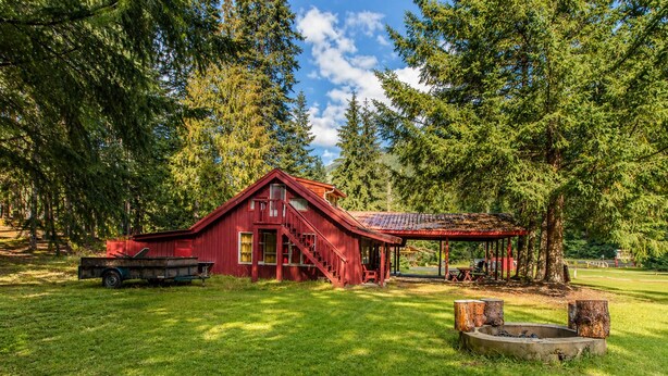A red barn with a covered porch, a truck, and a fire pit in a grassy area with trees.