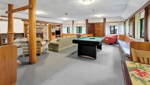 A pool table in a room with wooden pillars, a sofa, and a fireplace.