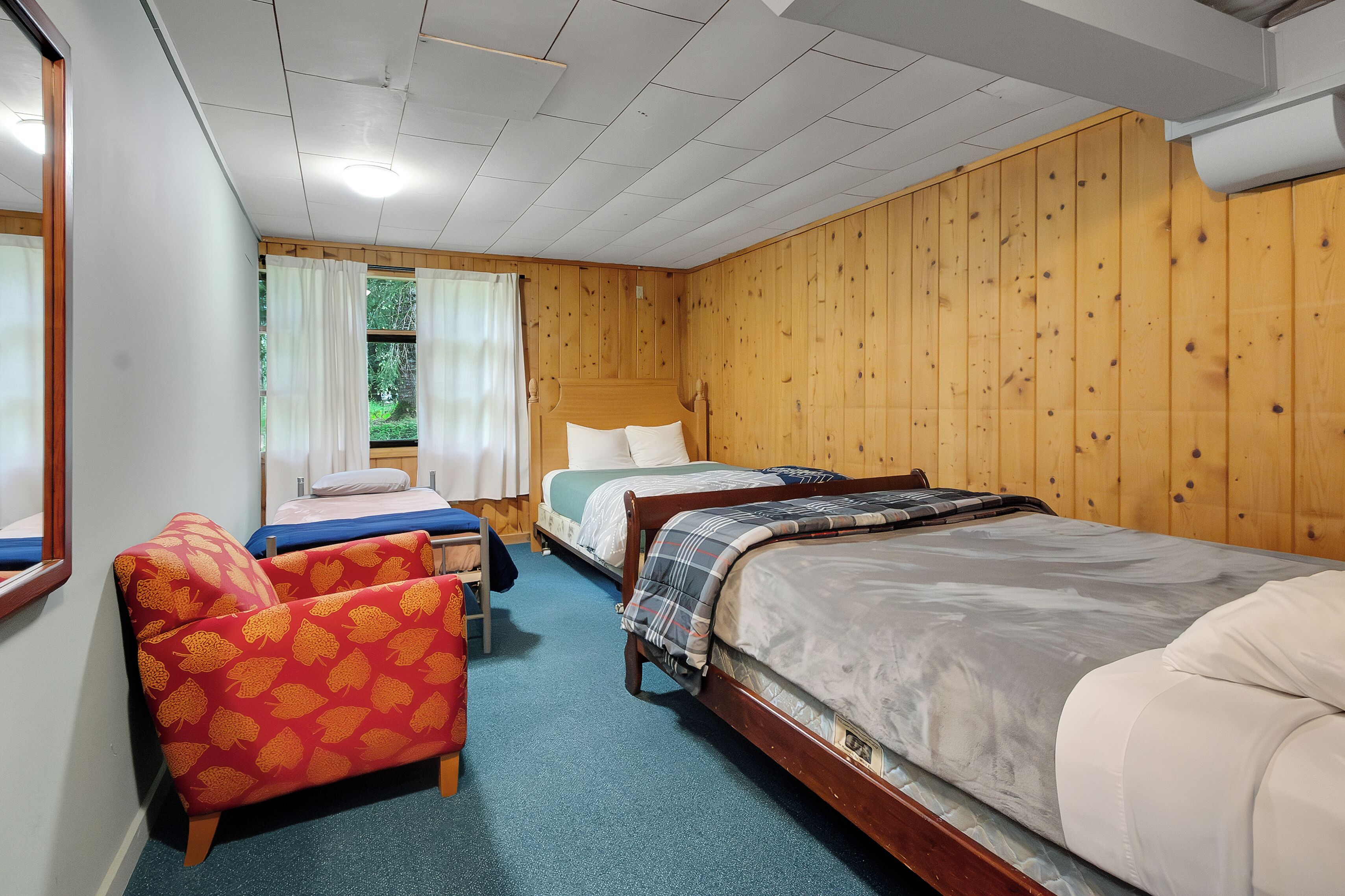 Une pièce avec trois lits, un mur en bois et une fenêtre avec des rideaux.