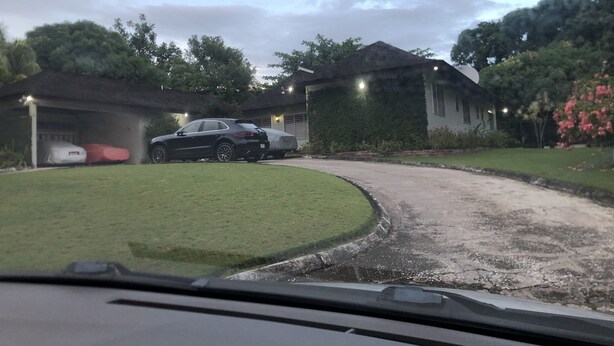 A residential driveway with a parked car, a garage, and a house with a covered porch. - Magic casa (Kingston)