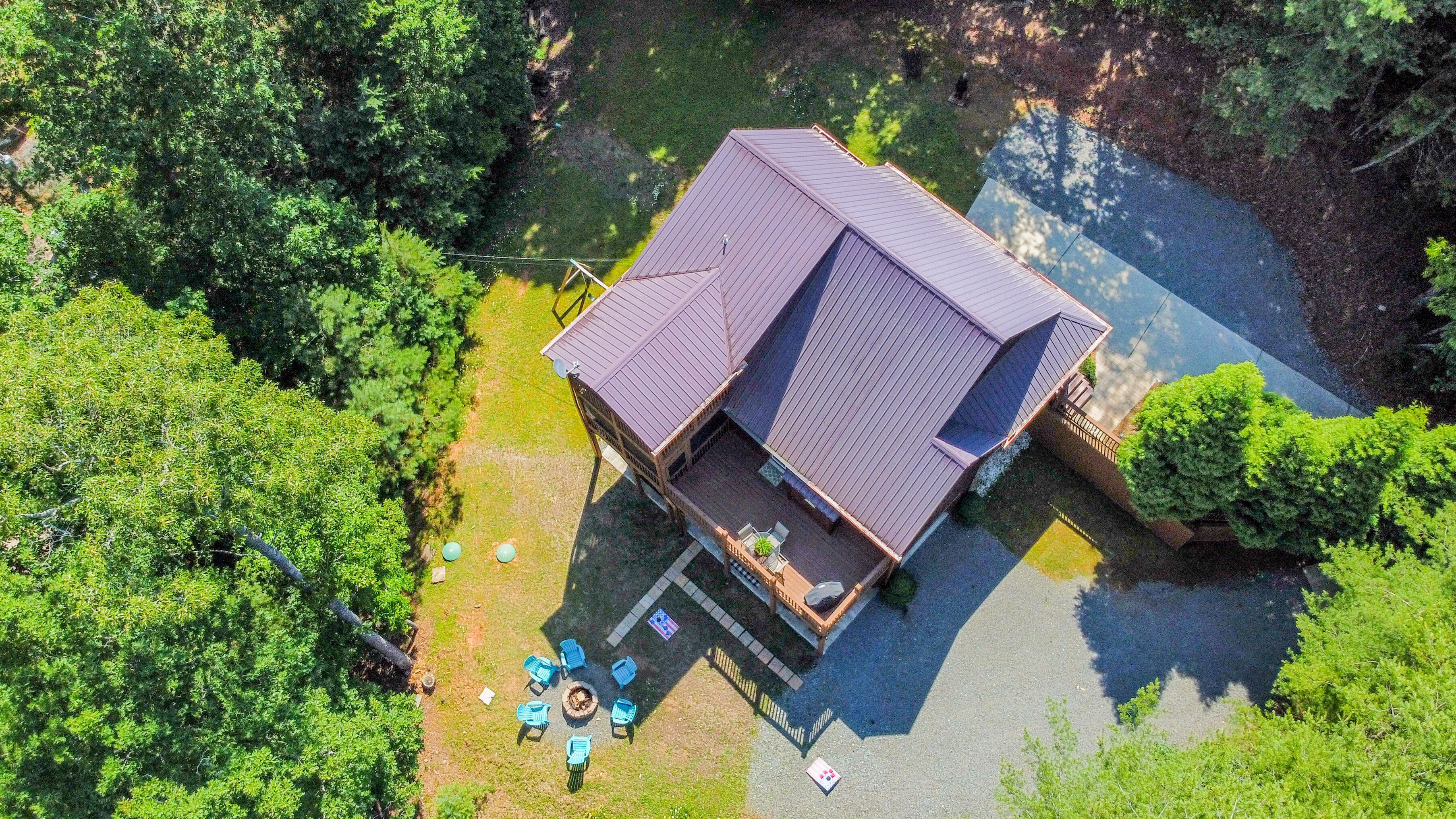An aerial view of a house with a sloped roof, surrounded by dense greenery.
