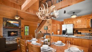 L’intérieur d’un chalet en bois comprend un coin repas, une cheminée, une cuisine et un escalier.
