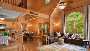 Un intérieur de cabine spacieux comprenant un coin repas, un canapé et une grande fenêtre donnant sur la forêt.