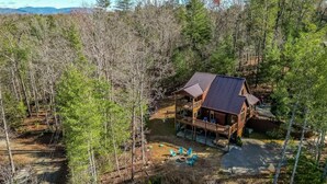 Une cabane dotée d’une terrasse et d’un patio couvert, entourée d’une forêt dense.