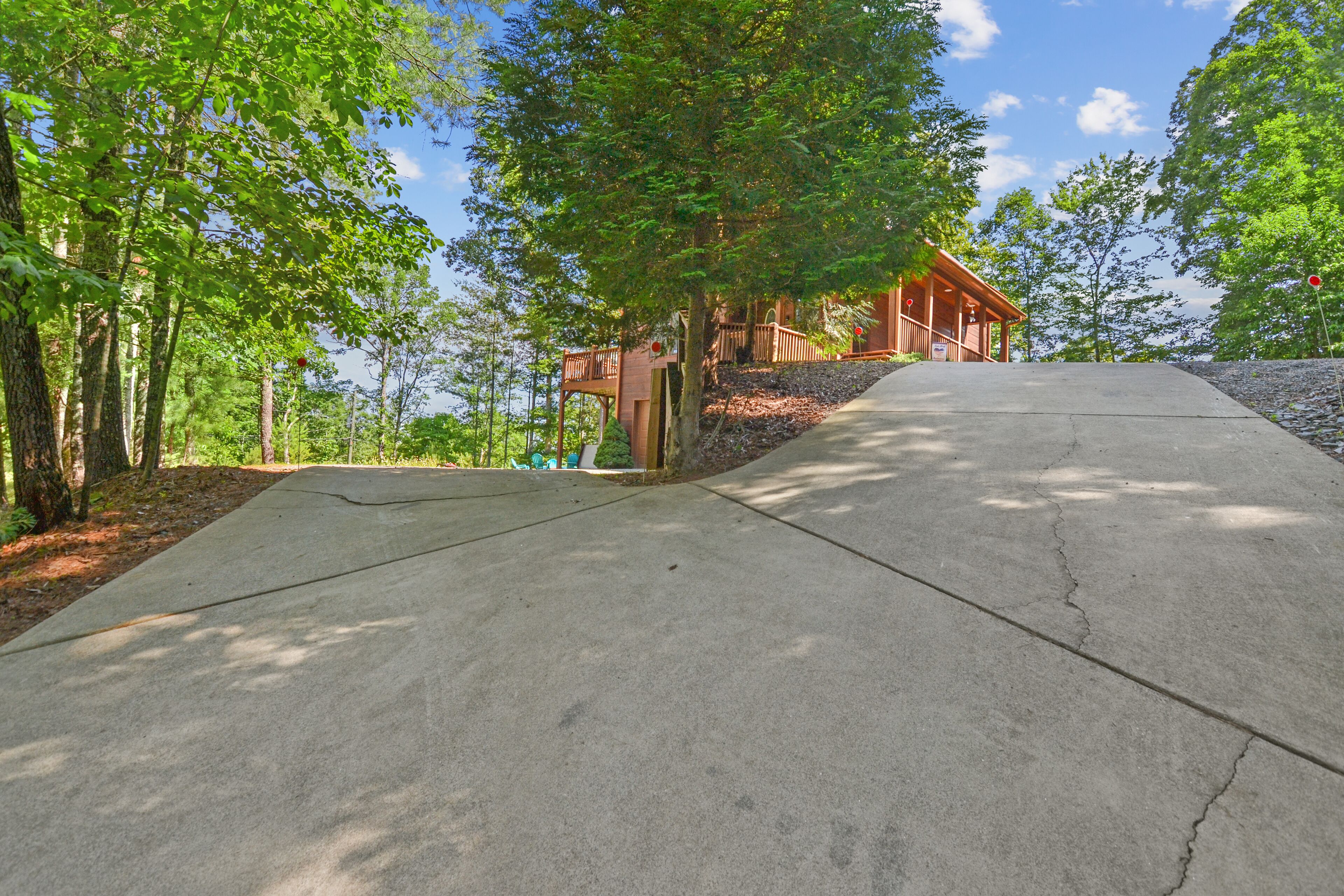 Ein Betonweg führt zu einer Holzhütte mit einer Terrasse, umgeben von Bäumen.