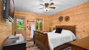 Une chambre à coucher située dans une cabane en bois, comprenant un lit, un ventilateur de plafond, une télévision et une porte donnant sur l’extérieur.