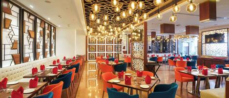Un restaurante con una decoración moderna, que presenta una amplia zona de comedor con mesas y sillas, un muro con diseño y un techo con luces colgantes.