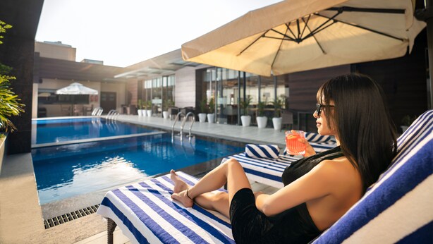 A person relaxing by a poolside lounge chair with a striped towel, a drink, and a sun umbrella. - Best Western Plus Chandigarh Mohali. (Mohali)