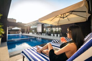 A person relaxing by a poolside lounge chair with a striped towel, a drink, and a sun umbrella. - Best Western Plus Chandigarh Mohali. (Mohali)