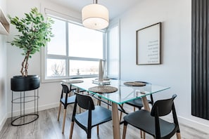 Un espace repas moderne avec une table en verre, des chaises noires, une plante en pot et une citation encadrée accrochée au mur.
