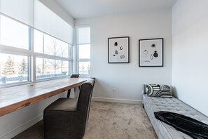 Une pièce comprenant un bureau en bois, un fauteuil rembourré, un canapé agrémenté de coussins à motifs et deux œuvres d’art encadrées accrochées au mur.