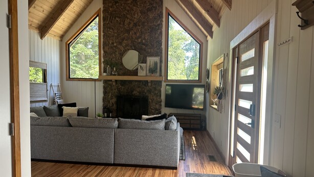 A cozy living room with a stone fireplace, a large gray sectional sofa, and a wooden floor.