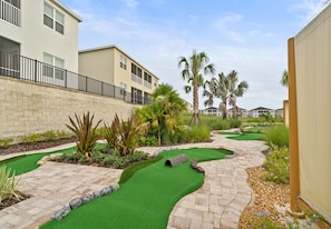 A residential area with a golf course, palm trees, and a brick pathway.