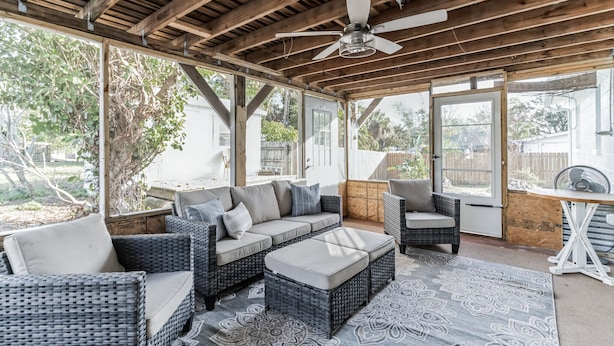 Ein überdachter Patio-Bereich mit Rattanmöbeln, einem Deckenventilator und einem gemusterten Teppich.