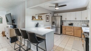 Eine moderne Küche mit Kochinsel, Barhocker, Kühlschrank und Deckenventilator.