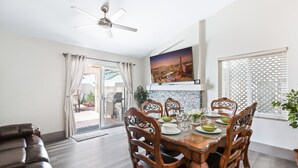 A dining area with a wooden table and chairs, a ceiling fan, and a cityscape painting on the wall.