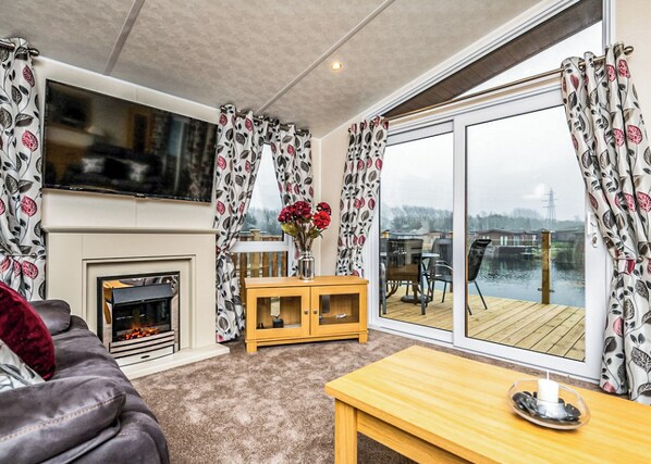A living room with a fireplace, a sofa, a wooden table, and a view of a lake through large windows.