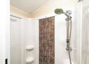 A shower with a rain showerhead and a handheld showerhead, a white wall with a brick pattern, and a door with a sign.