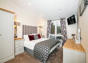 A bedroom with a bed, bedside tables, a desk, a TV, and a window with curtains.