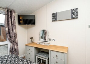 A bedroom with a bed, a vanity with a mirror, a television, and a patterned wall decoration. - 3 bedroom accommodation in Carnforth (Carnforth)