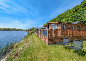 A lakeside wooden cabin with a deck, outdoor seating, and a view of the water.