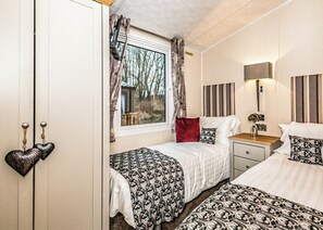 A bedroom with two beds, a window with curtains, a bedside table with a lamp, and a wardrobe with heart-shaped decorations. - 3 bedroom accommodation in Carnforth (Carnforth)