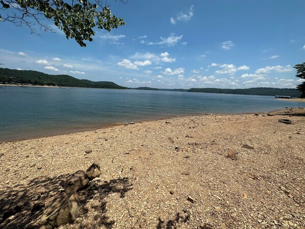 A pebbly beach with a calm lake, surrounded by hills.