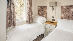 A bedroom with two beds, a bedside table with a lamp, and a window with curtains.