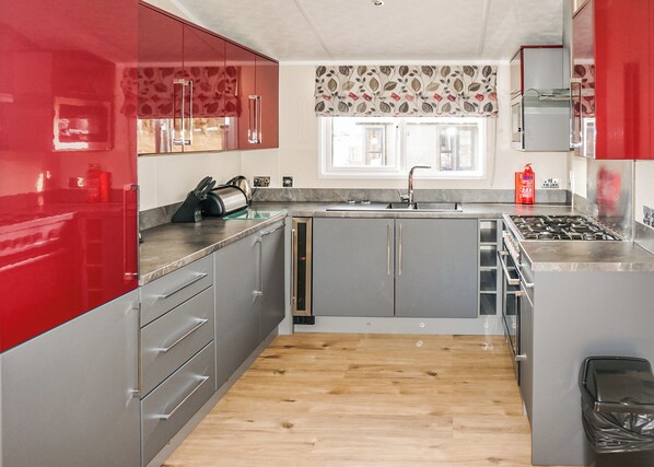 Une cuisine moderne avec des meubles gris, un mur d’accent rouge, un plancher en bois et une fenêtre ornée d’un rideau à motifs floraux.
