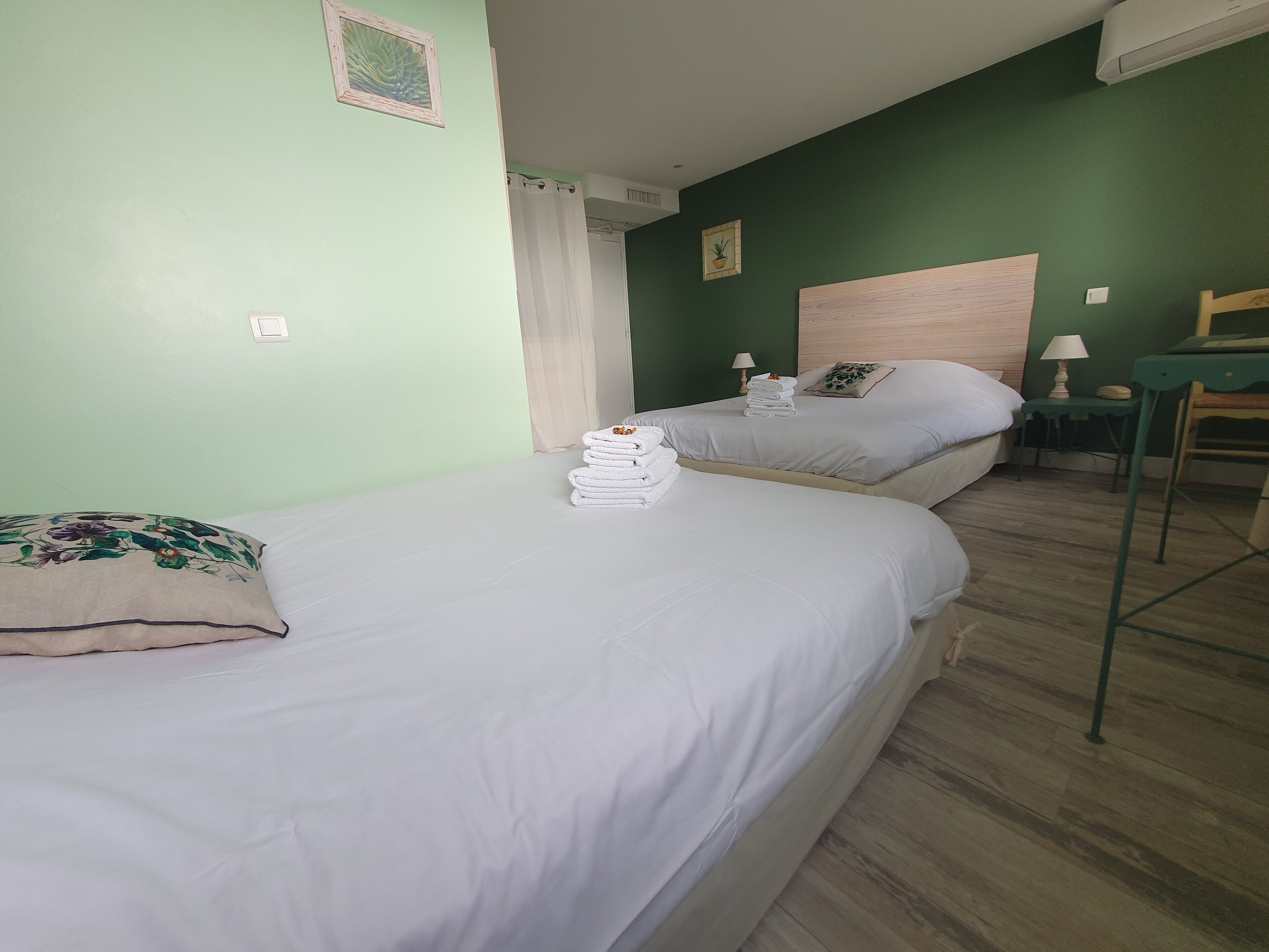 Habitación de hotel con dos camas, cabecero de madera, una mesita con lámpara y pared verde.