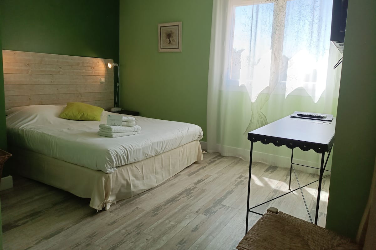 Ein Zimmer mit einem Bett, einem Nachttisch, einer Lampe, einem Fenster mit Vorhängen und einer Wand-Klimaanlage.