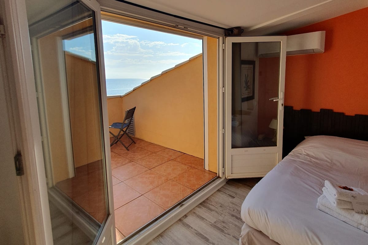 Ein Zimmer mit einem Bett, einer Schiebetür, die auf einen Balkon führt, und Meerblick.