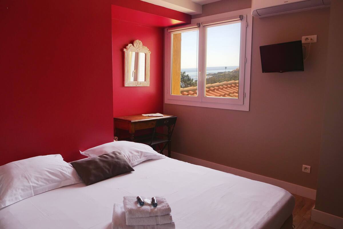 Ein Schlafzimmer mit Bett, Kissen, Schreibtisch, Stuhl, einem Fenster mit Blick und einem Fernseher an der Wand.
