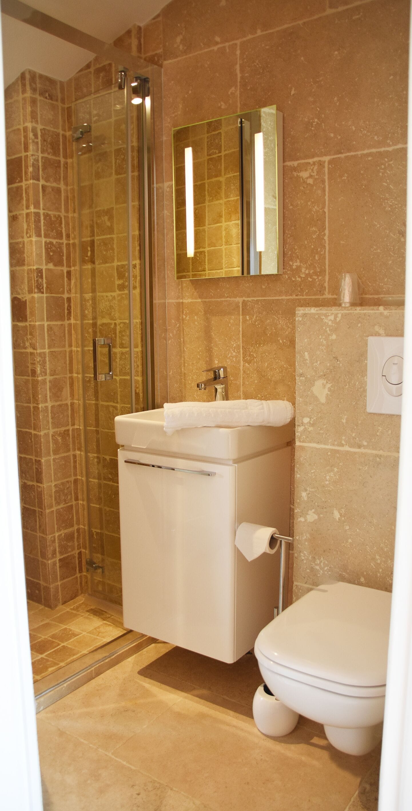 A bathroom with a glass-enclosed shower, a white sink with a towel, and a toilet.
