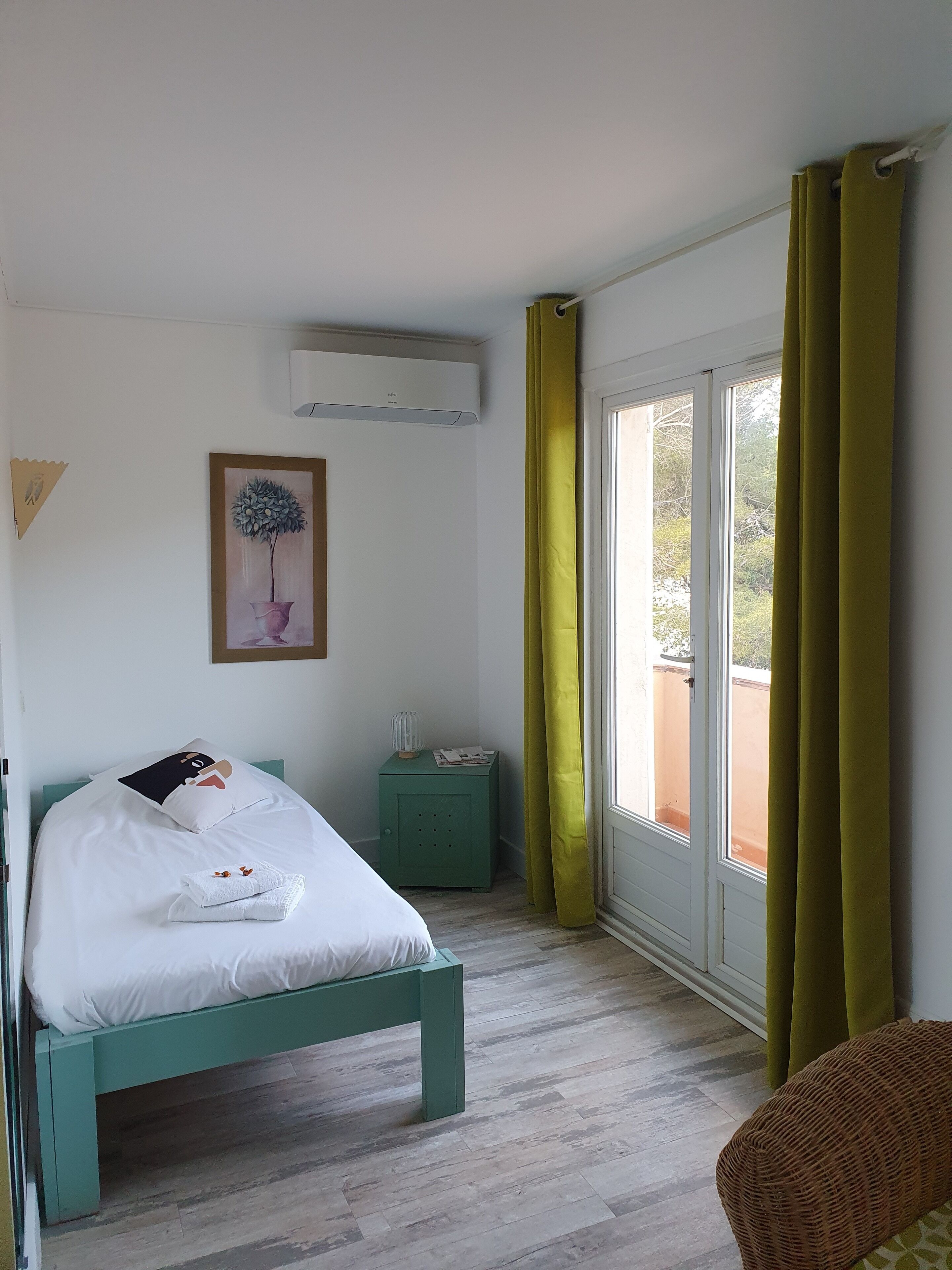 Un dormitorio con cama, mesita de noche, ventana con cortinas y aire acondicionado instalado en la pared.