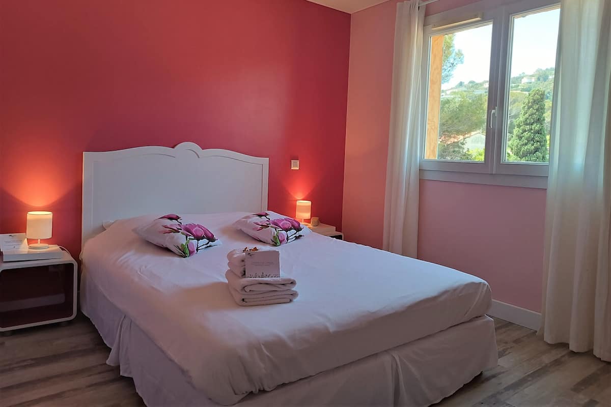 Ein Schlafzimmer mit einem weißen Bett, rosafarbenen Wänden und einem Fenster mit Vorhängen.