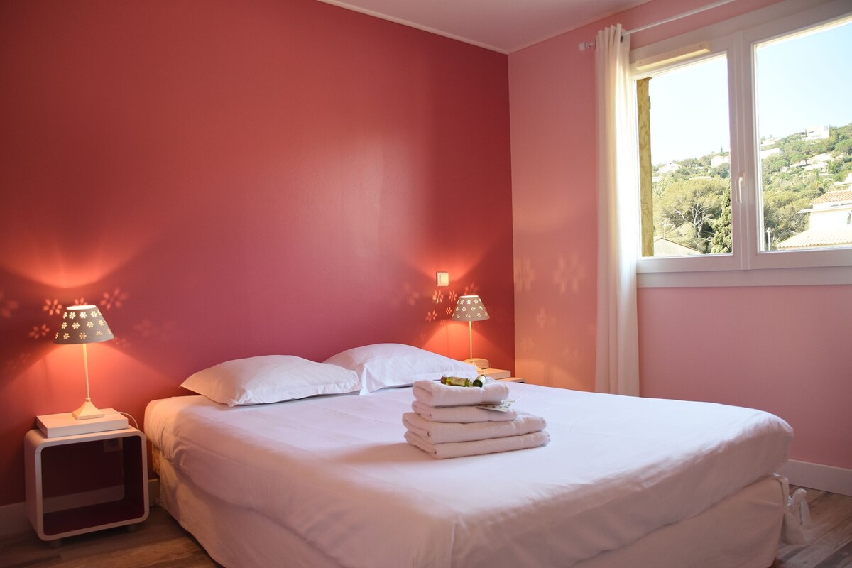 A bedroom with a bed, two bedside lamps, a window, and a view of a hillside.