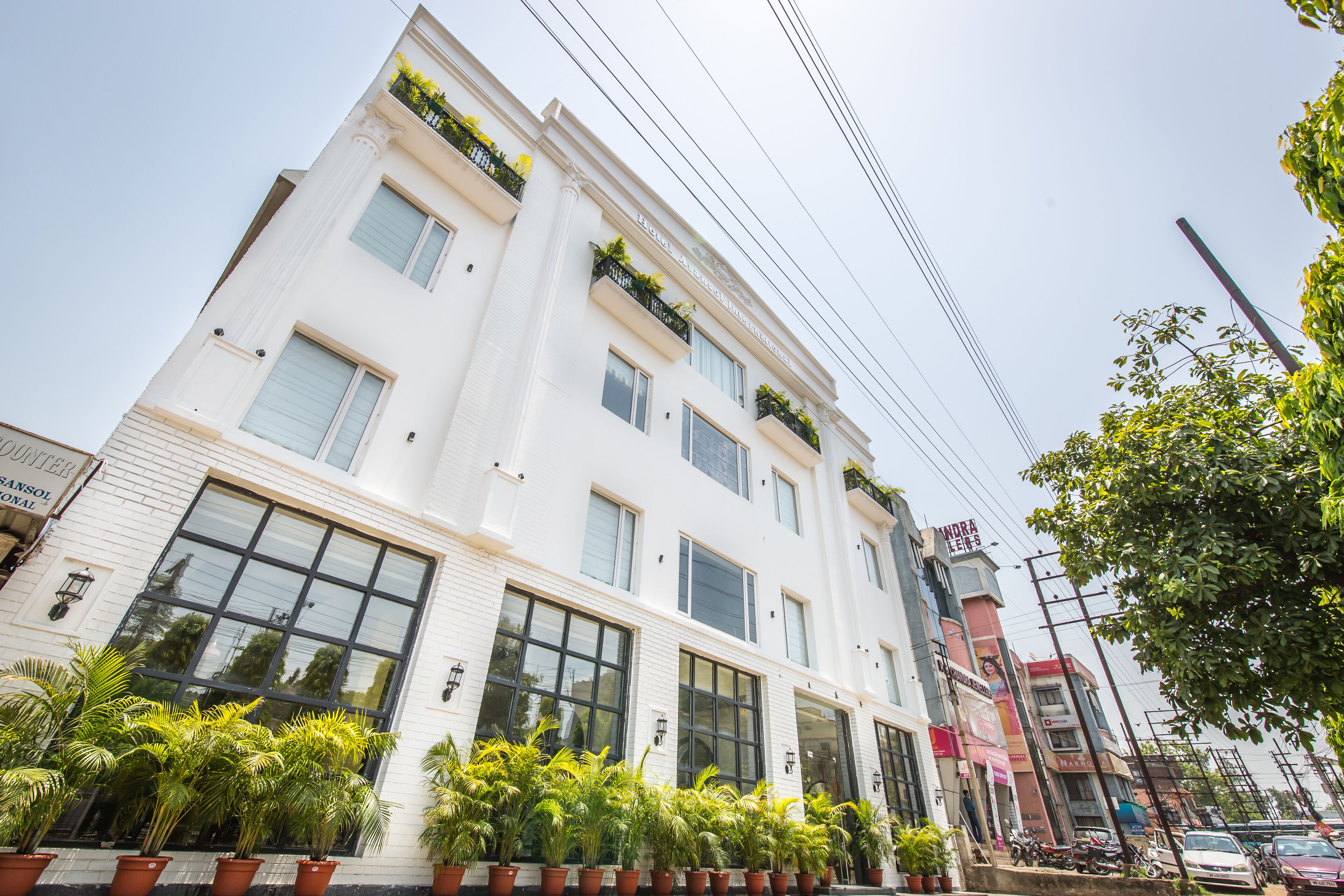 A multi-story hotel with large windows and balconies, surrounded by potted plants.