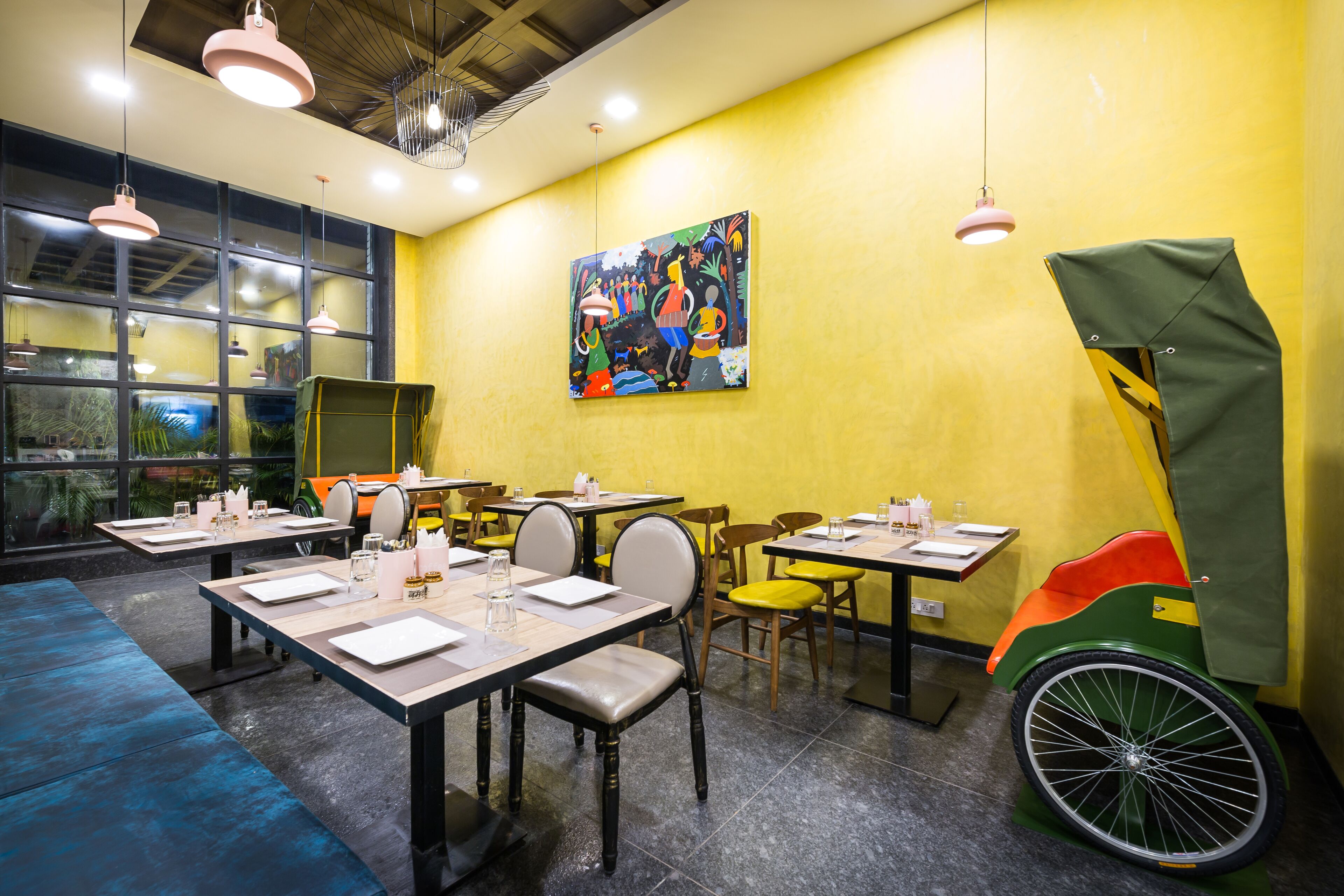A restaurant with tables set for dining, a colorful mural on the wall, and a bicycle-shaped chair.