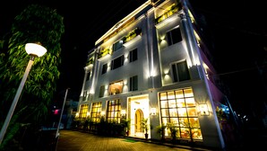 Een meerlaags hotel met verlichte ramen en balkons, een metselstenen pad en potplanten.
