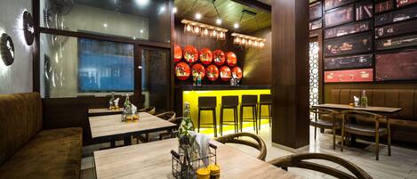 A restaurant interior with wooden tables, cushioned seating, and a wall of stacked suitcases.
