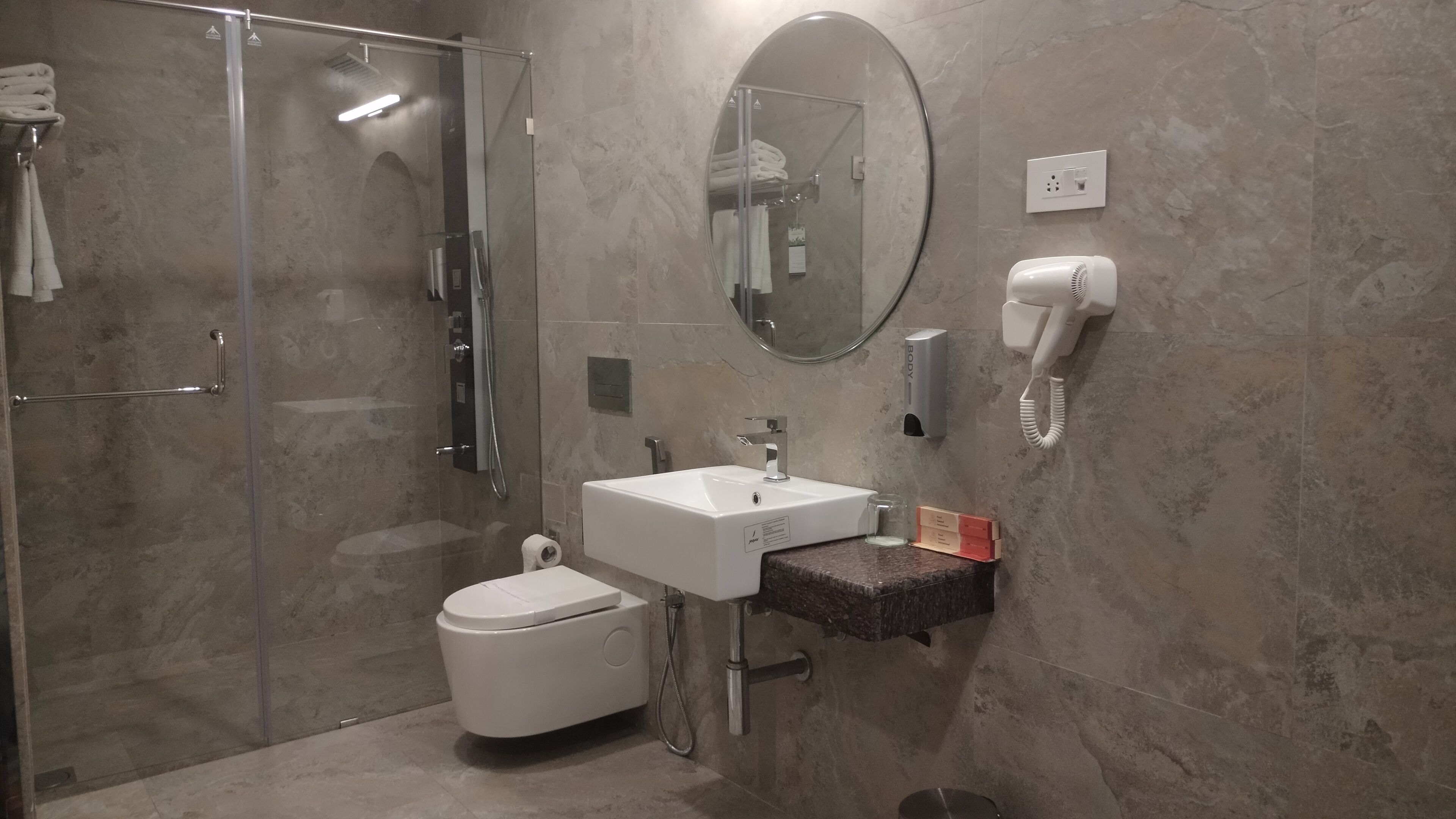 A modern bathroom with a glass-enclosed shower, a white toilet, a sink with a mirror above it, and a hairdryer mounted on the wall.